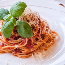 Makaron z sosem pomidorowym, posypany tartym serem, udekorowany liśćmi bazylii.