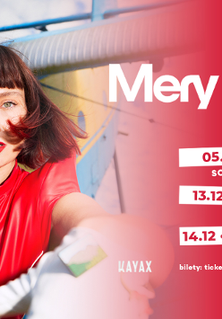 Kobieta zwrócona do obiektywu. Wyciąga dłoń. Ma krótkie brązowe włosy zakończone czerwonymi pasemkami. Ma na sobie czerwony kombinezon.