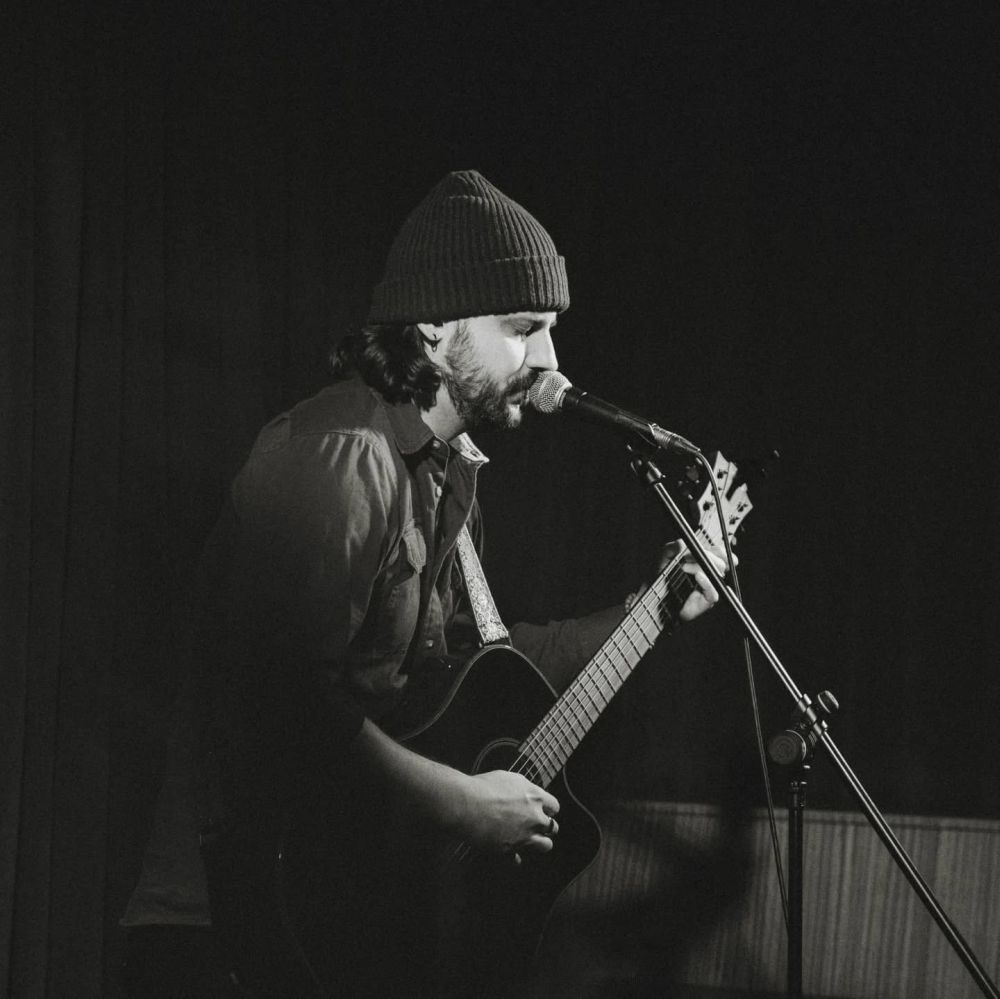 Mężczyzna w czapce gra na gitarze i śpiewa.