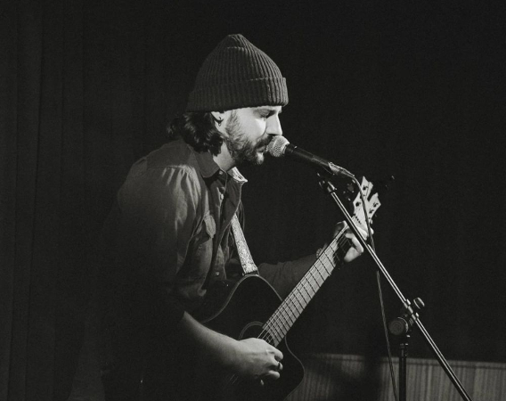 Mężczyzna w czapce gra na gitarze i śpiewa.