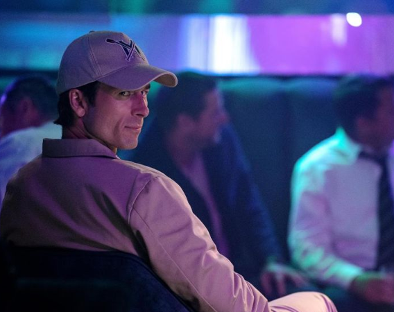 Mężczyzna w czapce z daszkiem odwraca się i spogląda na kogoś uważnie i przebiegle.