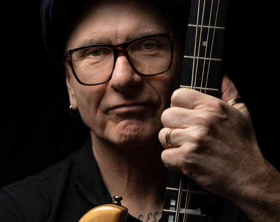 Mężczyzna w okularach pozuje z gitarą.