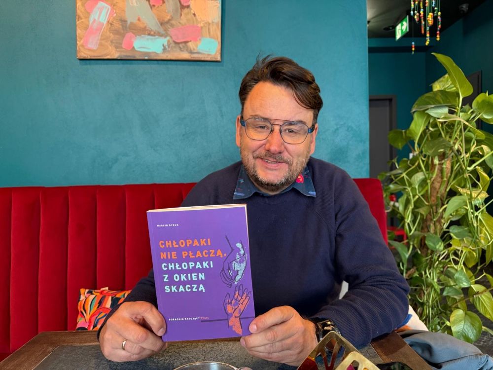 Mężczyzna w okularach trzyma w ręku książkę.