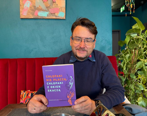 Mężczyzna w okularach trzyma w ręku książkę.