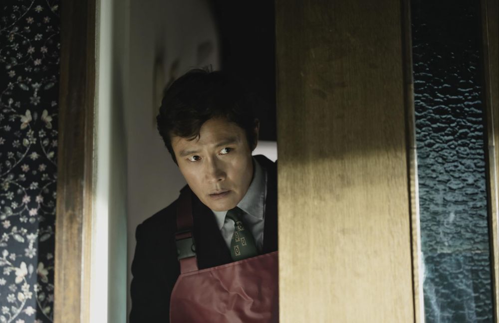 Mężczyzna w skórzanym fartuchu zerka zza drzwi.