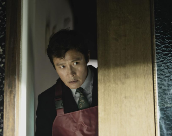 Mężczyzna w skórzanym fartuchu zerka zza drzwi.