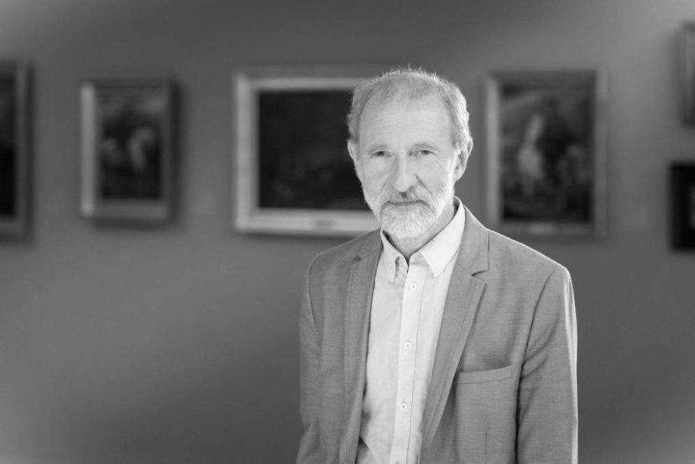 Mężczyzna z brodą na tle obrazów w muzeum.