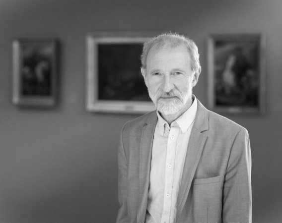 Mężczyzna z brodą na tle obrazów w muzeum.