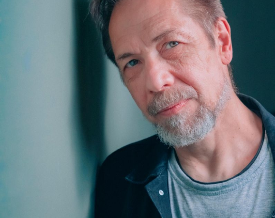 Mężczyzna z brodą opiera głowę o ścianę.