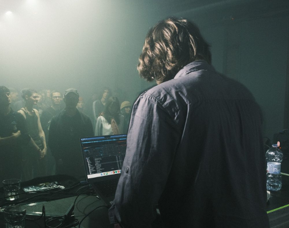 Mężczyzna za konsoletą gra koncert dla publiczności w klubie.