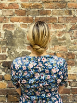 Kobieta stoi zwrócona przodem do ceglanej ściany.