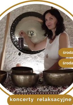 Kobieta w średnim wieku, w białej koszule, z czarnymi kręconymi włosami. Stoi przy rozłozonych złotych misach.