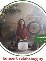 Zdjęcie przedstawia kobietę siedzącą przed dużym gongiem oraz kilkoma misami do śpiewu. Kobieta ma na sobie czerwoną koszulkę. Tło stanowi biała ściana. Kobieta ma ciemne włosy i patrzy w obiektyw aparatu. Kobieta lekko się uśmiecha.