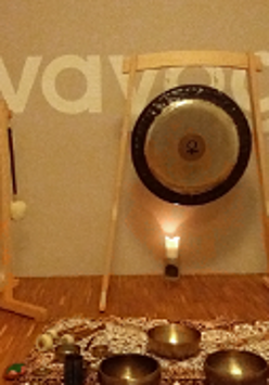 Zdjęcie przedstawia misy i gongi stojące pod ścianą, na której jest napisana nazwa miejsca koncertu na owe instrumenty, czyli Lovayoga.