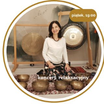 Kobieta w średnim wieku z czarnymi włosami. Ubrana w biały długi rękaw i wzorzyste spodnie. Siedzi na podłodze pokrytej dywanami. Za nią wiszą 2 gongi. Przed nią leży kilka mis.