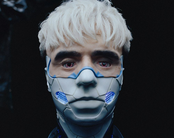 Młody mężczyzna w blond włosach z plastikową maską na dolnej połowie twarzy.