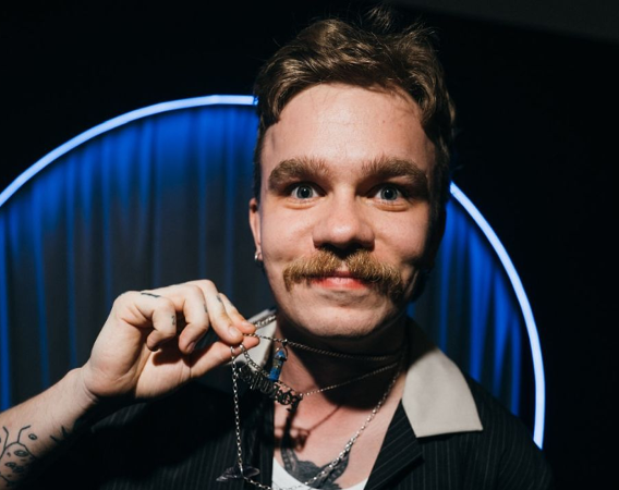 Młody mężczyzna z wąsem prezentuje swój wisiorek.