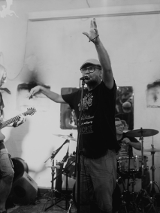 Czarnobiałe zdjęcie zespołu muzycznego składającego się z pięciu mężczyzn. Jeden śpiewa, dwóch gra na gitarach. Z tyłu jeden mężczyzna gra na perkusji a drugi na pianinie elektrycznym.