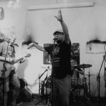 Czarnobiałe zdjęcie zespołu muzycznego składającego się z pięciu mężczyzn. Jeden śpiewa, dwóch gra na gitarach. Z tyłu jeden mężczyzna gra na perkusji a drugi na pianinie elektrycznym.