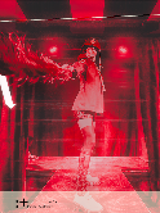 Obrazek informje o spektaklu Nasza racja. Widać na nim postać na scenie, oświetloną czerwonymi światłami.