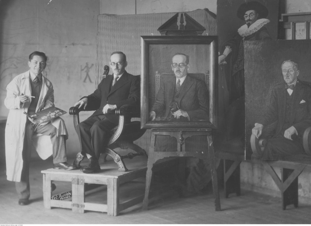 Czarno-biała fotografia, mężczyzna w okularach siedzi na podwyższeniu, pozuje malarzowi ubranemu w biały fartuch do portretu. - grafika artykułu