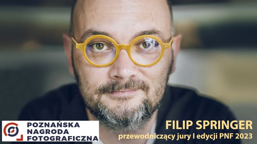 Zdjęcie przedstawia Filipa Springera, fotografa. Mężczyzna ma okulary w żółtych oprawkach, patrzy prosto w obiektyw.