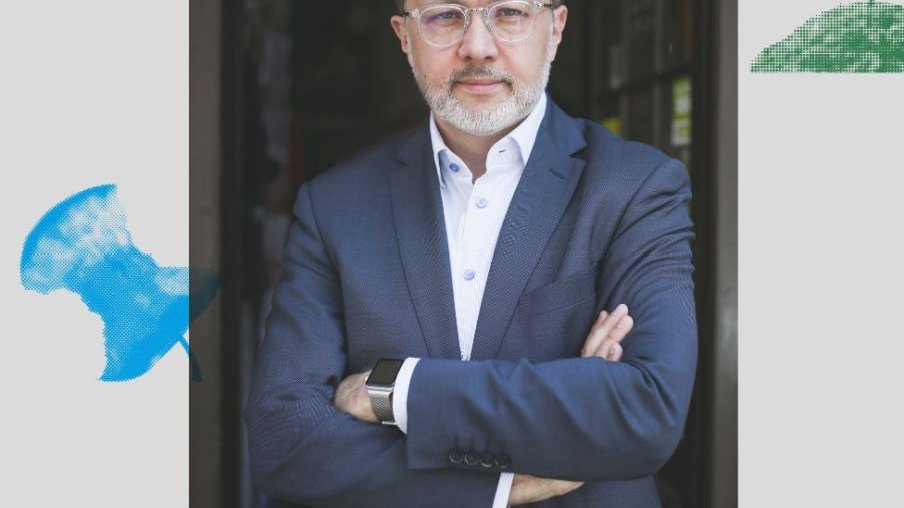 Michał Rusinek ma na sobie białą koszulę i granatowy garnitur. Patrzy prosto w obiektyw.