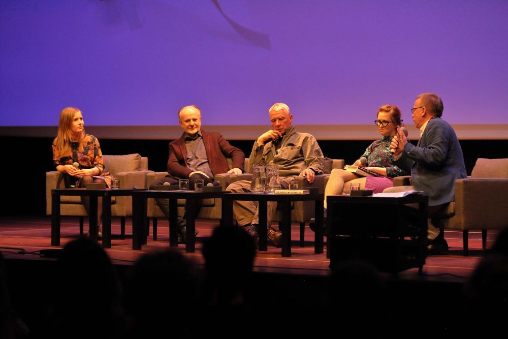 Na scenie siedzi czwórka gości spotkania, dwie poetki oraz dwóch poetów, z boku widać prowadzącego spotkanie profesora Piotra Śliwińskiego w granatowej marynarce. - grafika artykułu