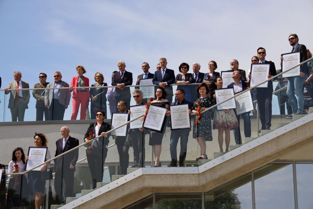 Na nowoczesnych schodach Muzeum Pierwszych Piastów na Lednicy stoją wszyscy laureaci Konkursu Izabella oraz inni muzealnicy. - grafika artykułu