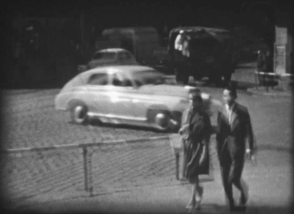 Poruszony, biało-czarny kadr z filmu 8-milimetrowego. Para idąca chodnikiem w pobliżu skrzyżowania, z tyłu jadące samochody. - grafika artykułu