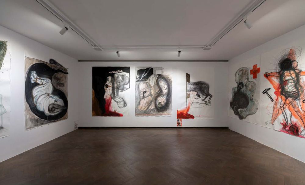 Wystawa "Anatomia polityczna". Pomieszczenie z trzema białymi ścianami, na których znajdują się obrazy operujące czernią, bielą i czerwienią - grafika artykułu