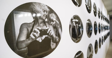 Zbliżenie na jedną z czarno-białych fotografii, widać na niej Izabellę Gustowską robiącą samej sobie zdjęcie w lustrze, aparatem analogowoym.