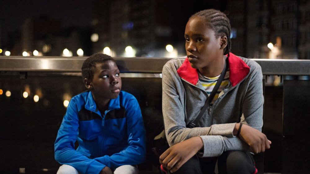 Dwójka głównych bohaterów filmu - czarnoskóra dziewczyna z warkoczykami oraz młodszy czarnoskóry chłopiec - siedzą na ławce, zamyśleni. Jest noc.