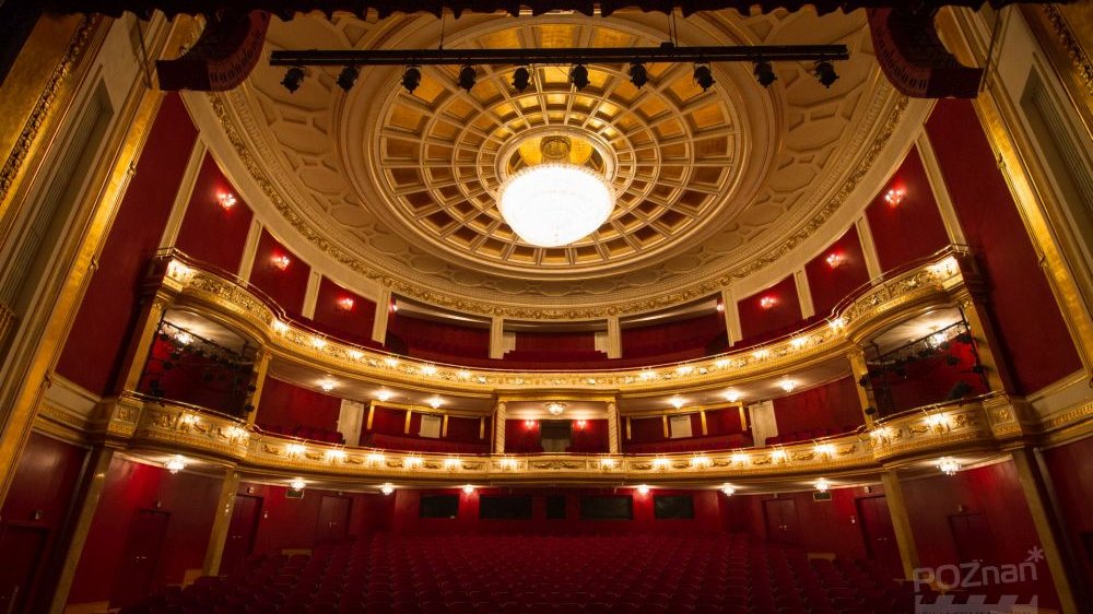 Rozświetlana sala w Teatrze Wielkim, dominują kolory złoto-czerwone, widać balkony, loże, widownię.