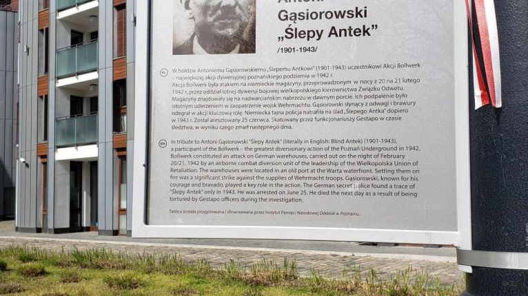 Na tablicy, któa stoi obok bloku, widać zdjęcie "Ślepego Antka" oraz tekst opisujący jego postać.
