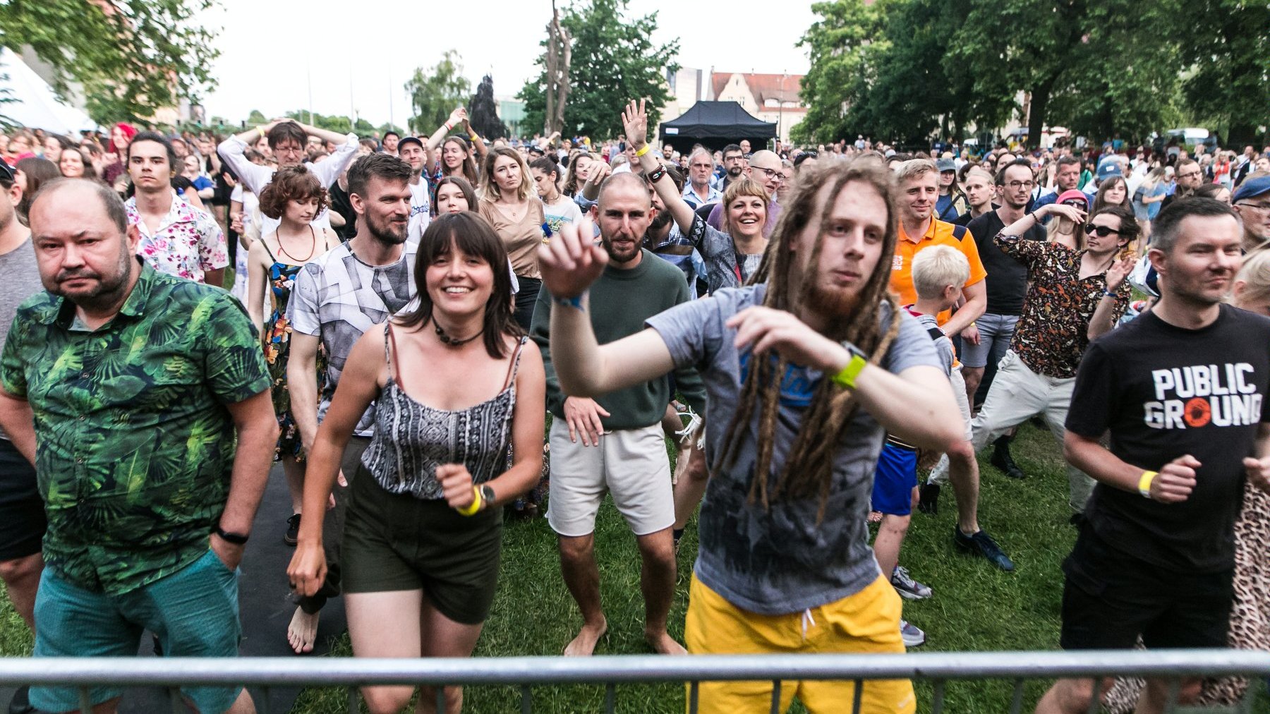 Publiczność koncertowa. Grupa ludzi stoi przed sceną i tańczy.