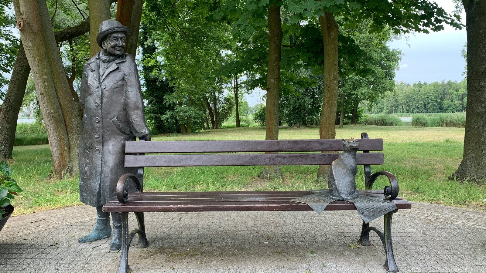 Uliczny pomnik w formie ławki, przy której po jednej stronie stoi podobizna Wisławy Szymborskiej, a po drugiej - kot.