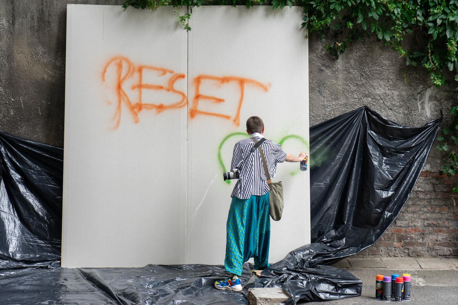 Dziewczyna stoi tyłem do obiektywu i sprayem rysuje napis "RESET" na białym płótnie. - grafika artykułu
