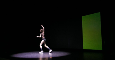 Podświetlony performer wykonuje taneczne ruchy na scenie.