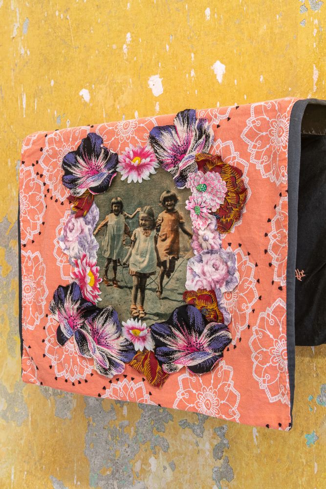 Kolorowa makatka przedstawiająca koloryzowane zdjęcie trzech małych dziewczynek w zabawie, otoczone wianuszkiem kwiatów. - grafika artykułu