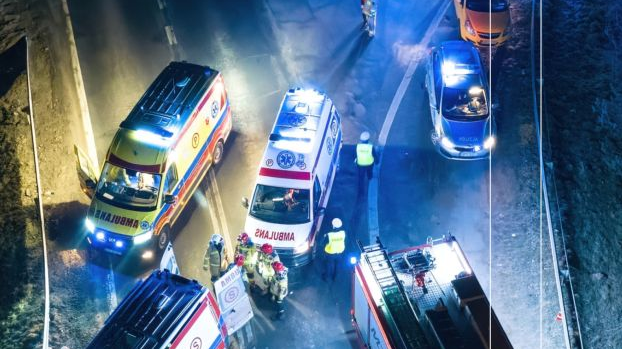 Fotografujący patrzy z góry na wypadek samochodowy - na drodze stoją dwa auta oraz kilka karetek, wokół pojazdów kręcą się funkcjonariusze.