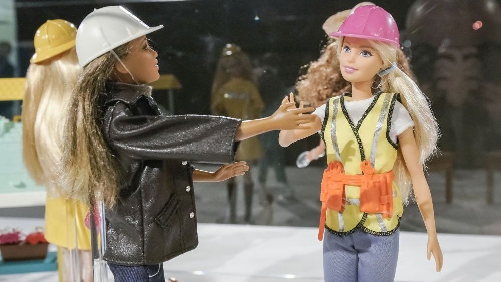 Lalki Barbie w strojach i kaskach pracowników budowlanych w szklanej gablocie.