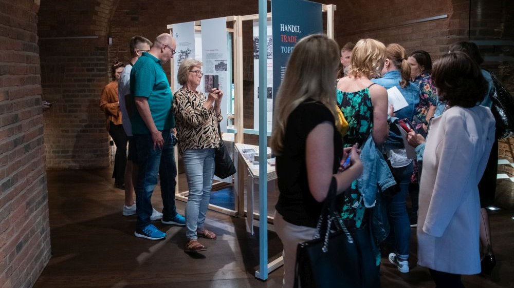 Liczna grupa zwiedzających na wystawie, chodzą między planszami z opisami poszczególnych zagadnień.