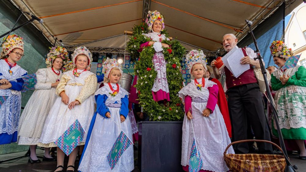 Ludzie w strojach bamberskich stoją na zadaszonej scenie. Z przodu wiklinowy kosz i mikrofon.