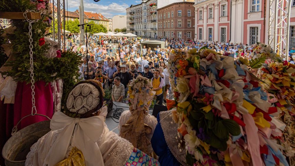 Tłumy ludzi pod sceną na świeżym powietrzu. Na scenie ludzie w strojach bamberskich stojący tyłem do fotografa.