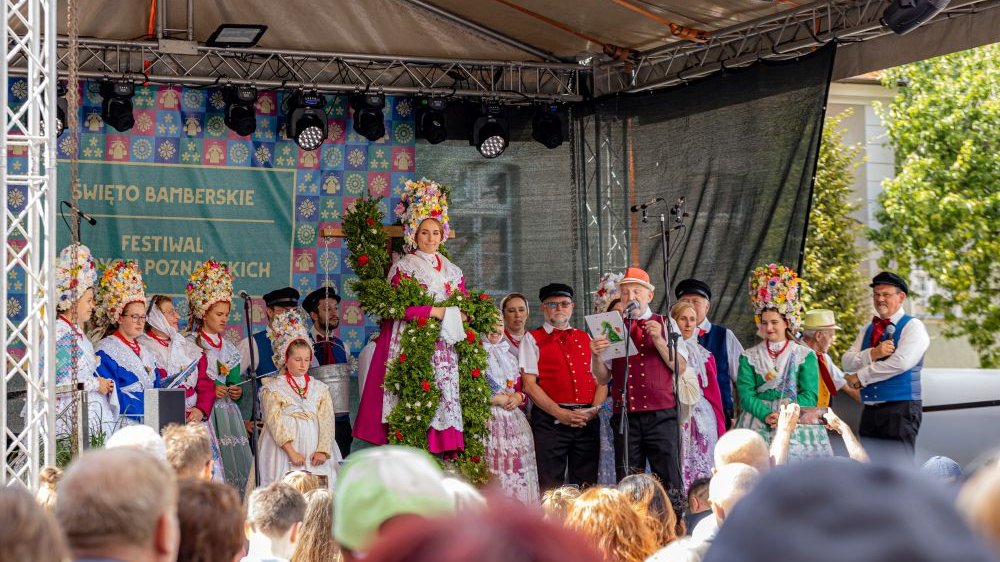 Ludzie w strojach bamberskich stoją na zadaszonej scenie. Pod sceną publiczność.