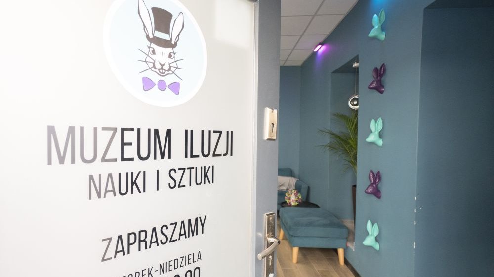 Drzwi do Muzeum Iluzji, na którym widać logo z białym królikiem oraz godziny otwarcia muzeum (wtorek-niedziela, 10-19).