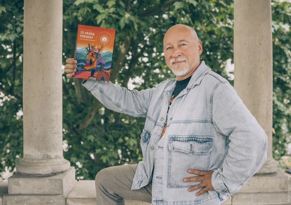 Autor ma na sobie dżinsową, błękitną kurtkę, stoi w humorystycznej pozie odkrywcy, a w prawej ręce trzyma książkę. - grafika artykułu