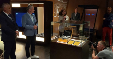 Prezentacja najnowszego eksponatu w Centrum Szyfrów Enigma. Dookoła szklanej gabloty stoją ludzie, m.in. wiceprezydent Poznania Jędrzej Solarski.
