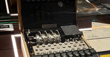 Enigma z bliska. Widzimy metalowe elementy mechanizmu, w tym klawisze z alfabetem i koła zębate.